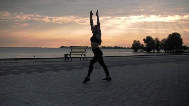 Young woman doing backflips.Girl doing acrobatic activity against the sea at sunrise. Fitness Lifestyle slow motion.