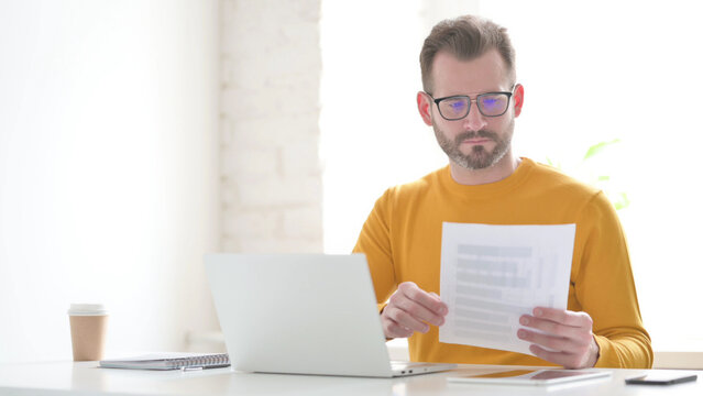 Man with Laptop Reading Documents in Office