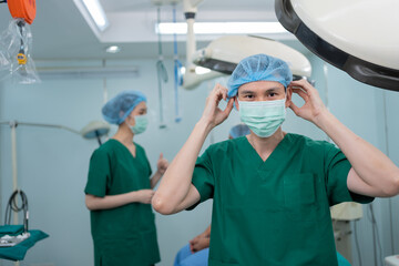 Portrait of Asian surgeon with medical mask standing in operation theater at a hospital. Team of...