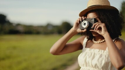 4k Portrait of attractive african-american woman in hat making photos on retro camera in the summer field. Countryside and farmland style.
