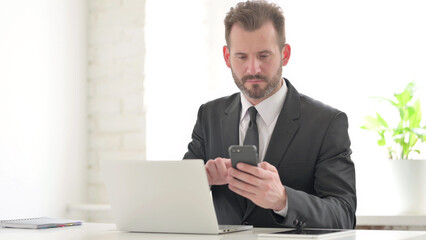 Young Businessman using Smartphone while using Laptop in Office