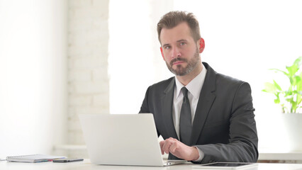 Young Businessman Looking at Camera while using Laptop in Office