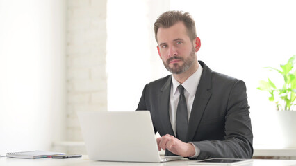 Fototapeta premium Young Businessman Looking at Camera while using Laptop in Office
