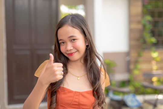 A girl in her late teens poses for the camera while she gestures a thumbs up. Signaling that she is fine.