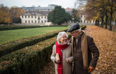 Happy senior couple on walk outdoors in town park in autumn.