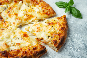 Italian pizza four cheeses with stretching cheese and basil on a light concrete background