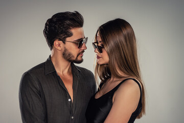 Portrait of young handsome couple wearing fashionable sunglasses, looking at eachother. Bearded man...