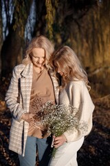 Fototapeta premium Adult daughter hugs her pregnant mom while standing in autumn park