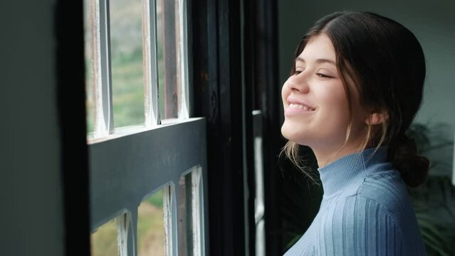 One young woman looking at the window having fun and relaxing cloudy day at home alone. Female person feeling good indoor.