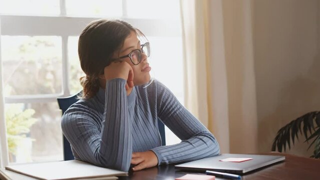 One beautiful female teenager sleeping and resting on the table while studying or working at home. Millennial taking a break after doing homework using laptop.
