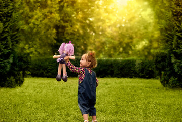 Cute little girl playing with her favorite doll outdoors in a summer park.