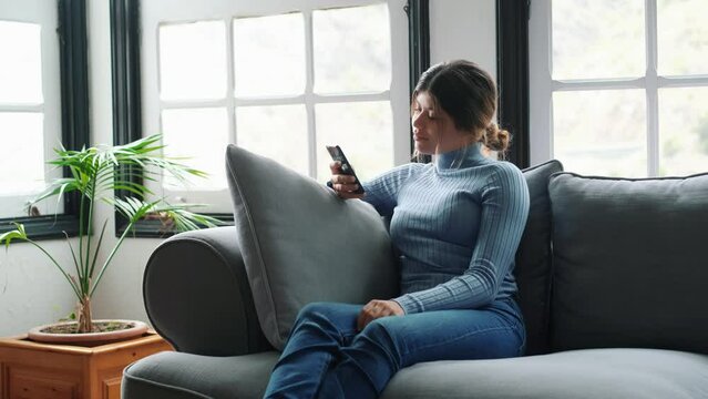 Young beautiful woman sitting on the sofa at home chatting and surfing the net. Female person having fun with smartphone online. Portrait of girl smiling using cellphone revising social media
