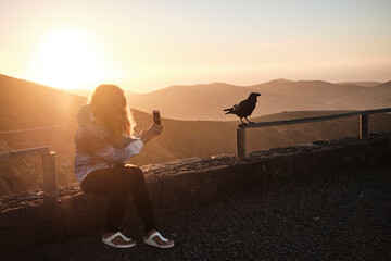 Person photographing crow in the sunset in the mountains
