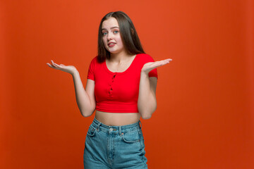 Puzzled young girl shrugging shoulders, dont know answer, uncertain with information on orange background