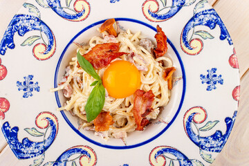 Carbonara pasta with bacon and chanterelles in a decorative plate.