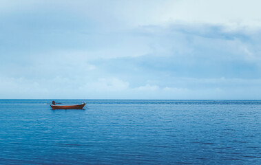 A small red fishing boat floating alone in the sea. Calm blue water and clear skies.