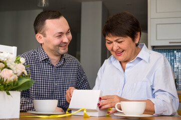 Holiday celebration concept. Suprized smiling senior woman holding gift sitting near her adult son. Spring holidays.8 march,birthday, mother's day