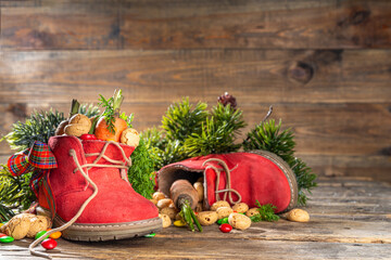 Sinterklaas, Saint Nicholas day background. Little kid red shoe with carrots and sweets, trooigoed, pepernoten, candy. Dutch Christmas holiday on cozy wooden background.