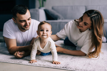 Young mother and father standing in their living room at home affectionately cradling the cute baby...