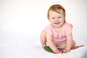Fototapeta premium A wonderful cute little baby girl with red hair plays and laughs. Birthmark. Hemangioma. White background, space for text. Lifestyle.