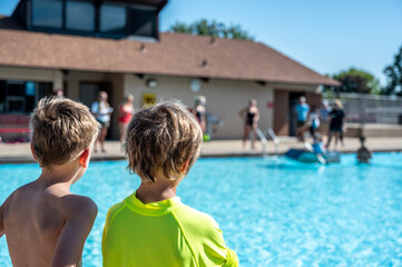 Fototapeta na wymiar Two boys looking towards a cardboard boat floating in a pool.