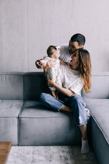 Naklejka premium Proud mother and father smiling at newborn baby daughter, sitting on the sofa at home