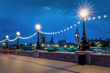 Lampposts illuminated at night on the Queen's Walk, view on Westminster palace and Big Ben in...