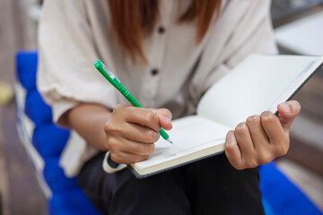 The girl's hand holding a pen is writing down something on a notebook.