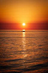Obraz premium sunset over the sea with rigged inflatable boat RIB crossing through the sunlight reflection