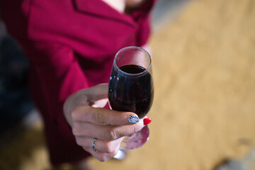 Young and beautiful businesswoman posing in her wine cellar in front of wooden wine barrels. The woman holds in her hands a glass of wine from her harvest and shows it to the camera. wine concept