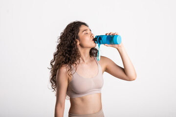 Resting time. Sporty girl with towel on shoulders drink water. Photo of muscular fitness model isolated on white background. Health concept