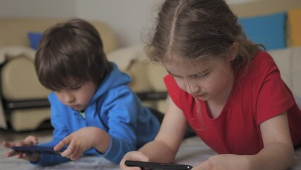 Children Playing Games In Phone at Home Lying on Floor. Kids Playing Video Game on Mobile Phone. Boy and Girl Plays Video Game Smartphone. Friends Using Phone for Gaming Online Education Social Media.