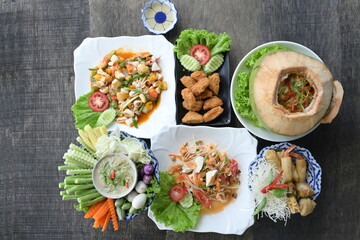A variety of Thai dishes are laid out on wooden tables :Papaya salad,seafood wrapped in coconut,stir-fried squid with salted egg,simmered soy bean paste with fresh vegetables,fried chicken,spring roll