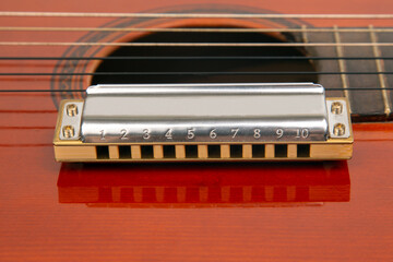 The harmonica rests on the body of a classical guitar. Classical musical wind instrument. - obrazy, fototapety, plakaty