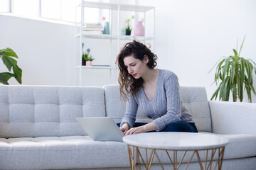 Satisfied caucasian woman working on comfortable couch, using laptop at home, happy girl chatting with friends in social network, spending lazy weekend, watching movie, shopping online, writing email