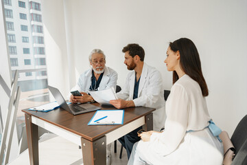 Fototapeta premium Two doctors in white uniform consult female patient at meeting in private clinic. High quality photo