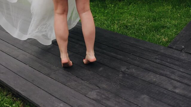 Shooting the legs of a girl who is spinning around herself on a wooden path in the park. In her hands is a white dress