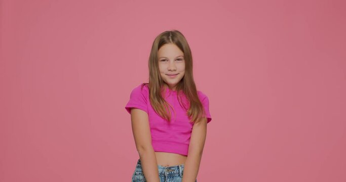 Embarrassed shy cute little girl blogger showing embarrassment gesture on pink studio background. Medium shot