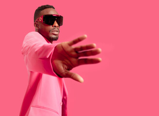 Horizontal portrait of african man with fashionable pink sunglasses and jacket posing on pink background. Copy space