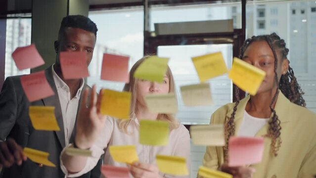 work in office, three people of different races are discussing new project, sticking post-it notes