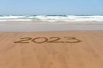 Year 2023 written in the sand on the beach with the sea in the background