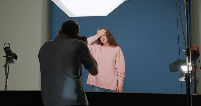 Backstage of advertising photo shooting. Photographer takes photos of actress showing headache in studio