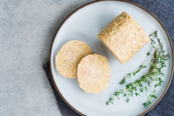 Top view raw Tempeh or Tempeh, made of fermented soybean seeds. Tempeh Slices on plate with herbs. Soya protein. Plant based meat concept. Healthy Cooking and eating. Go vegan. Flat Lay, copy space