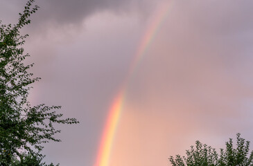 Close up view of rainbow in cloudy evening summer sky.
