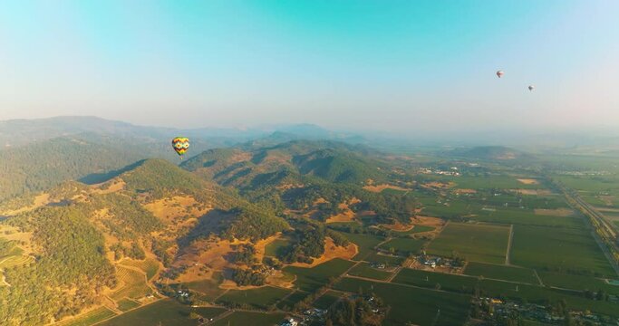 Three hot air balloons in the clear blue skies over amazing scenery. Flying aerostats in green valley of Napa, California, USA.