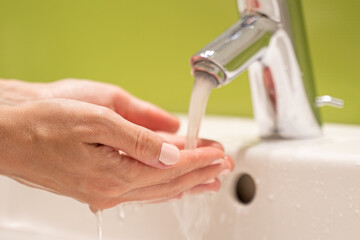 Woman with nice manicure washes hands over sink turning on water. Tourist takes care of herself washing hands from bacteria and viruses closeup