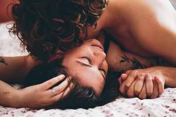 Young passionate couple kissing for intense sex in the bedroom at home, tender lover likes to touch the soft skin of a sexy sensual tattooed lady moaning and making love, foreplay concept (day time)
