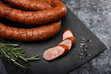 Smoked sausage in rings on black stone background. Composition with traditional Polish meat cold...