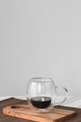 Bubble glass cup of black coffe on a wooden board on a tablecloth. Copy sapace, front view.