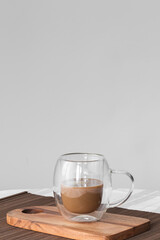 Bubble glass cup of coffe with milk on a wooden board on a tablecloth. Copy sapace, front view.